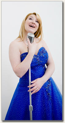 Chantal Dupuis chantant dans un micro d’époque, en robe bleue